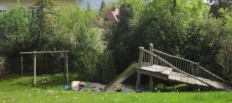 Hausgarten der Familie N mit einer Rutsche, Sandkasten und einer Schaukel