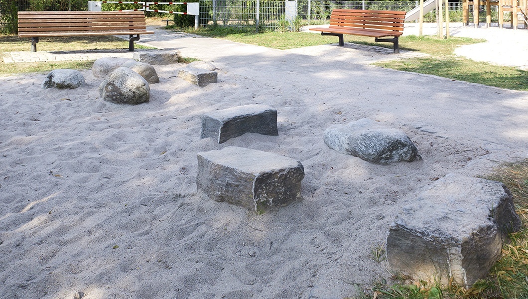 Foto vom Sandkasten mit Sand und großen Steinen auf dem Spielplatz im Lauter Park